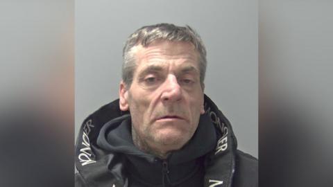 A man in a black hooded sweatshirt and black jacket. The collar of the jack has some white lettering on the inside. 