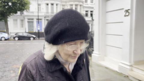 Dr Ann Coxon wearing a black beanie and black jacket walking along a street