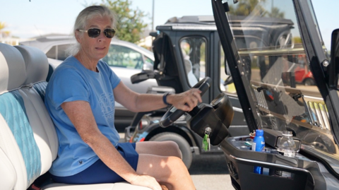 Maddy Bacher in a golf cart wearing sunglasses and a blue tank-top