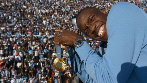 An image of Letsile Tebogo holding a gold medal in front of a crowd