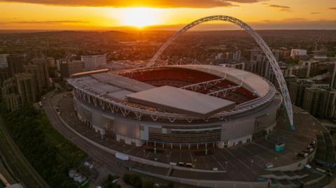 An aerial view image of Wembley stadium at sunset, surrounded by houses and tower blocks. 