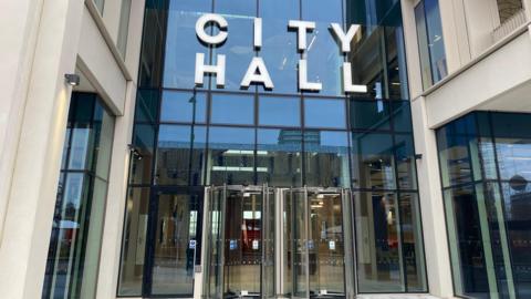 Sunderland City Council's headquarters. The glass fronted building has two revolving doors at its entrance. The words CITY HALL sit above the doors.