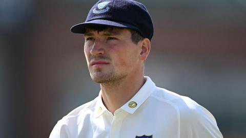 Henry Crocombe looks on in white Sussex shirt and dark blue Sussex cap