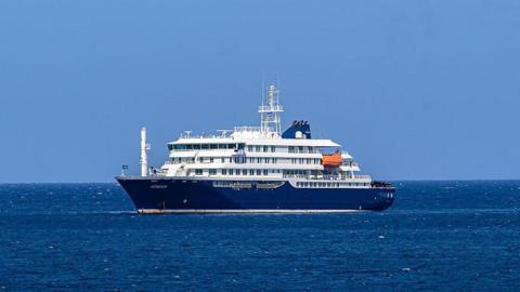The blue and white cruise ship MV Hondius stationary in the ocean off the port of Praia, the capital of Cape Verde.