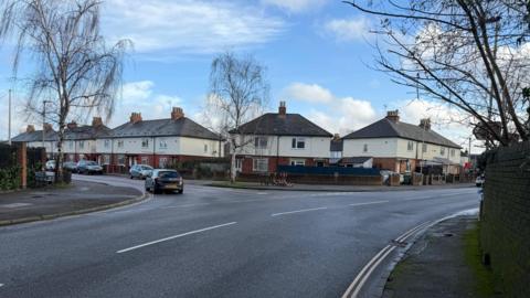 Google maps street view of St Paul's Road and the junction for Folly Lane in Cheltenham. There are cars on the road and houses on the street. 