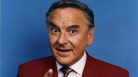 Bob Monkhouse in a suit pointing at the camera