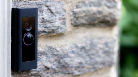 A black doorbell camera mounted on a stone wall which is out of focus. 