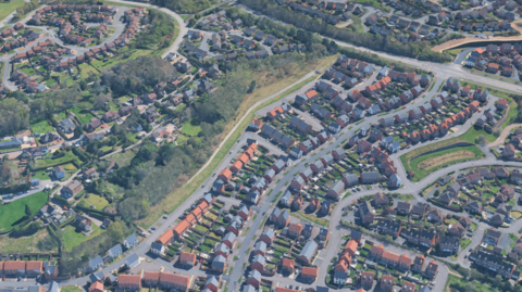 A aerial view of houses, bounded by roads and green space in Telford that includes trees.