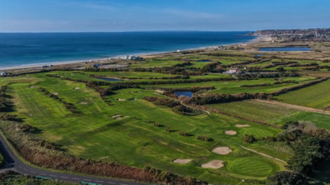An aerial image of the golf course with the sea visible in the background. 