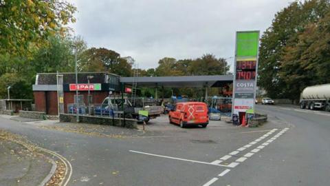 St Austell Services - a petrol station just off a roundabout in Cornwall. An orange van is driving into the petrol station, which is going through refurbishment work with workmen and fencing up around the site.