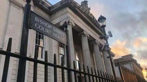 Bishop Street Courthouse in Derry. A grey building can be seen behind black railings. A sign reads: 'Bishop Street Courthouse'