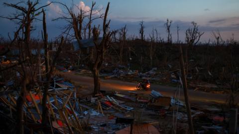People ride a bike among debris in an area with no light in the aftermath of Hurricane Melissa in Auchindown, Saint Elizabeth Parish, Jamaica, November 4,