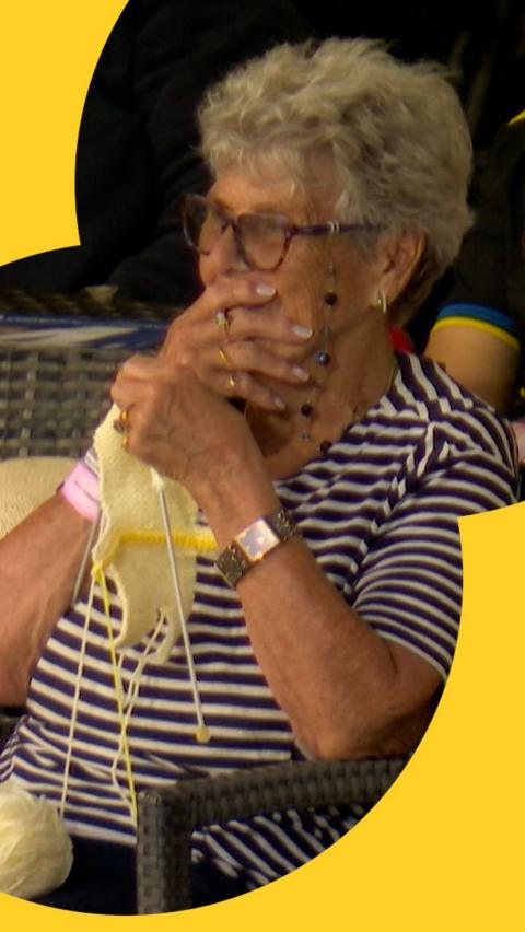 A fan in the crowd covers her mouth in shock at appearing on the big screen at Emirates Old Trafford while knitting