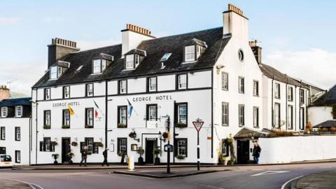 The George Hotel - a large hotel with white painted walls, flags hanging outside and people walking past it