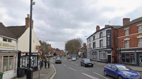 Road with a blue car at the front of the photo, with green traffic lights just beyond
