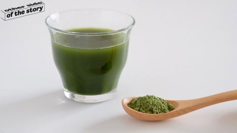 Glass of diluted greens powder and a spoon with greens powder