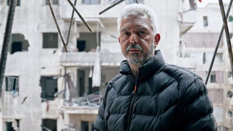 Middle-aged man, Mohammed, in ruins of wrecked apartment block