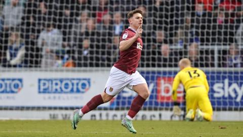 Sam Hoskins wears white shorts and a maroon football top, the colours of Northampton Town