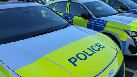 Three police cars with yellow, blue and white colours, parked in a row