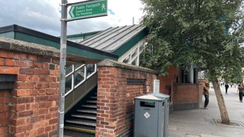 A street entrance to Nottingham station featuring a gap in a brick wall, a footpath sign and steps leading up into a covered walkway