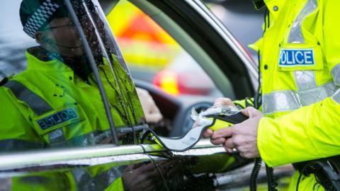 A police officer preparing a breathalyser test in a car window. The driver cannot be seen but the window is down, and only the police officer's torso can be seen.
