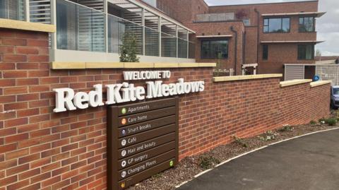 The entrance sign for Red Kite Meadows. It is on the wall of the extensive modern brick-built building.