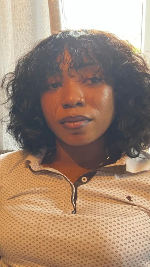 A woman with curly brown hair wearing a cream tshirt