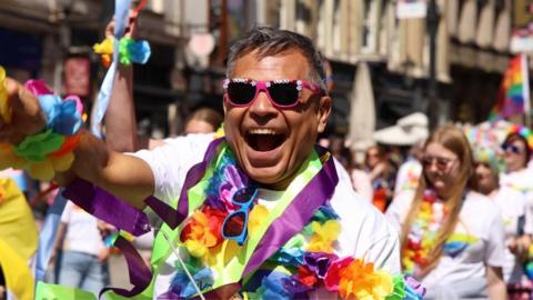 A man wearing sunglasses and colourful items with a large smile
