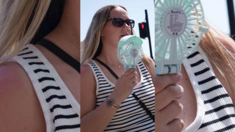A woman cooling her face with a battery powered fan