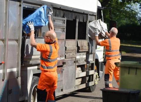 two bin men working collection refuse and tipping bags into a bin lorry. 