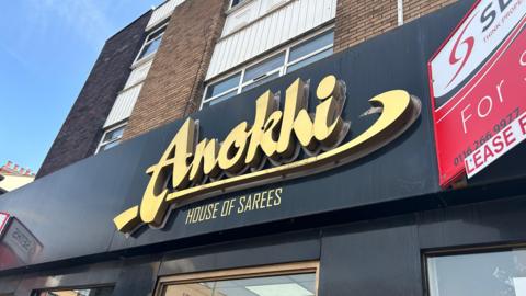 A shopfront with the words Anokhi House of Sarees in gold lettering