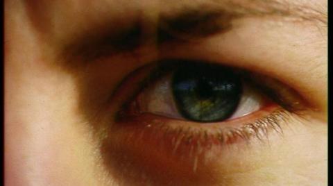 Close-up of a Caucasian person's right eye. The eyebrow and nose are in frame but out of focus while the eye itself is in focus, showing a blue pupil surrounded by dark eyelashes. 