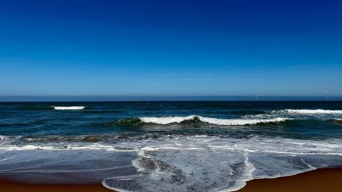 Waves gently rolling in to a sandy shore with bright blue sky above