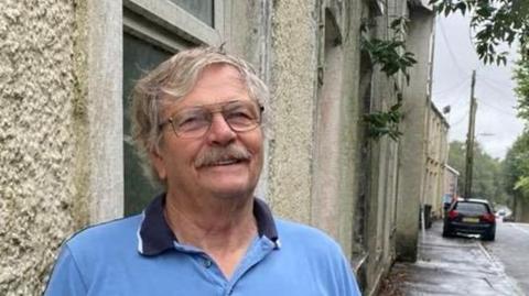 Gabe Thomas, in a blue shirt, standing outside one of the houses in Cyfyng Road