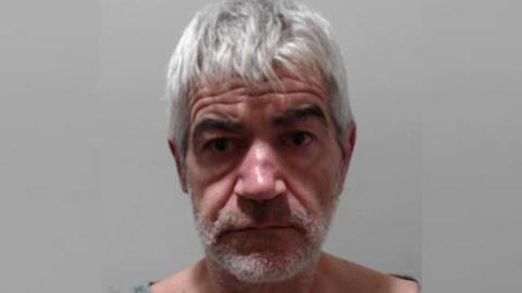 A police photo of William Lewis, a bearded man with white-gray hair and a lined forehead.