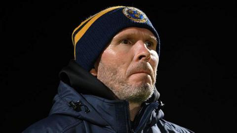 Shrewsbury Town manager Michael Appleton in his club beanie hat watches on from the touchline