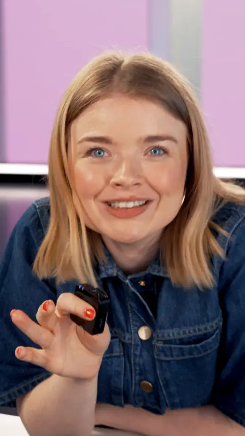 Woman with short blonde hair wearing blue denim dress and holding a small microphone