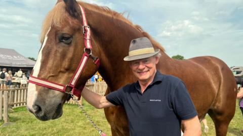 Martin Clunes is standing next to a horse wearing a hat and T-shirt.