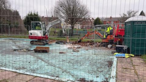 A white and red digger in a swimming pool behind a metal fence