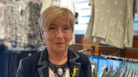 Winnie Mellett standing in her clothes shop in Ballymoney, with tops on rails behind her.