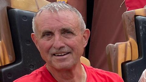 Headshot photo of a man with short grey hair wearing a red T-shirt