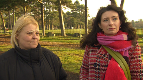 Two women being interviewed for television, standing in their local park which has deteriorated and had some play equipment removed.