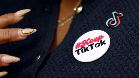 A woman with long nails wears a badge reading "Keep TikTok" on her top.