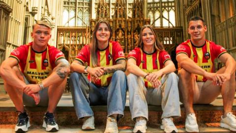 Four people smiling into the camera wearing the red and yellow striped football shirts. 