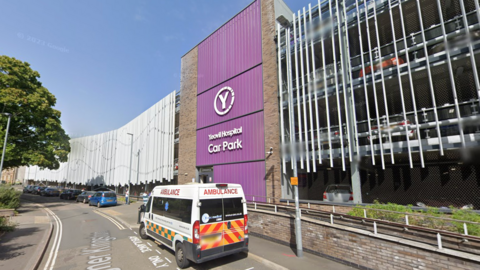 Yeovil Hospital multi-storey car park. The car park has a purple entrance sign. An ambulance is parked outside. 