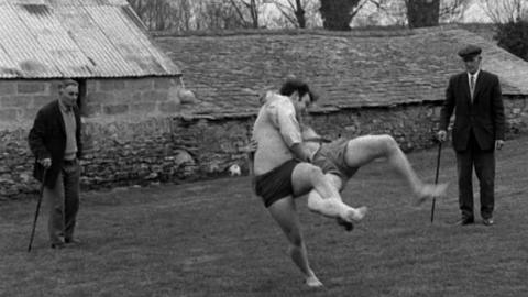 Two of the Chapmans wrestling while two men watch.