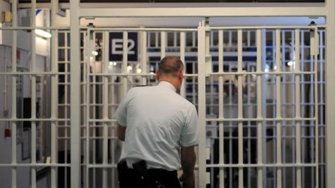 Male prison guard locks a white internal prison door. His back is to the camera.