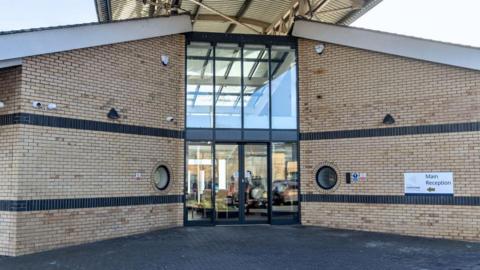 Front entrance of Hamptons Hospital, it is a yellow-brick building with glass-fronted entrance doors.