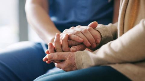 A stock photo of a close up of two people holding hands in a supportive way. 