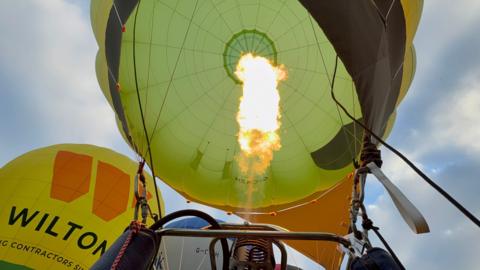 The inside of an inflated hot air balloon. A flame is centre. The balloon is green in colour.